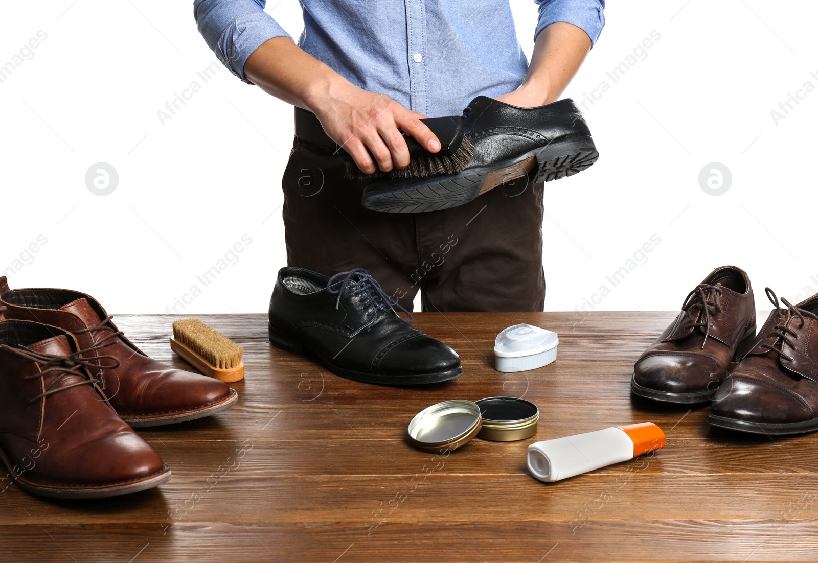 Photo of Man cleaning leather shoe at wooden table against white background, closeup