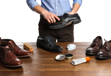 Photo of Man cleaning leather shoe at wooden table against white background, closeup