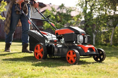 Photo of Man cutting green grass with lawn mower in garden, closeup