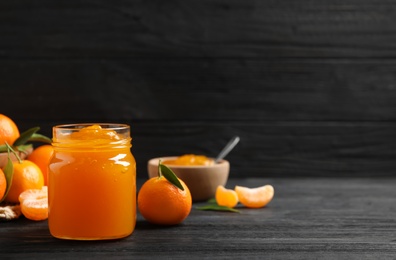 Tasty tangerine jam in glass jar on dark wooden table. Space for text