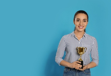Photo of Portrait of happy young woman with gold trophy cup on blue background, space for text