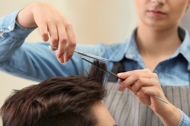 Photo of Barber making stylish haircut with professional scissors in beauty salon, closeup