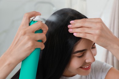 Photo of Woman applying dry shampoo onto her hair indoors, closeup