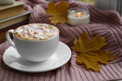 Photo of Cup of tasty hot drink with marshmallows near books, leaves and burning candle on blanket, closeup. Autumn coziness