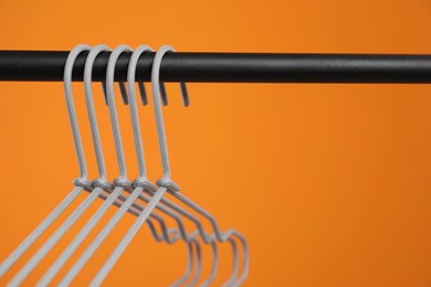 Photo of Empty clothes hangers on rack against orange background, closeup. Space for text