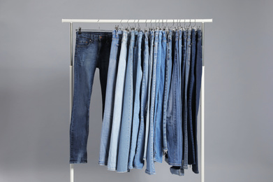 Rack with different jeans on grey background