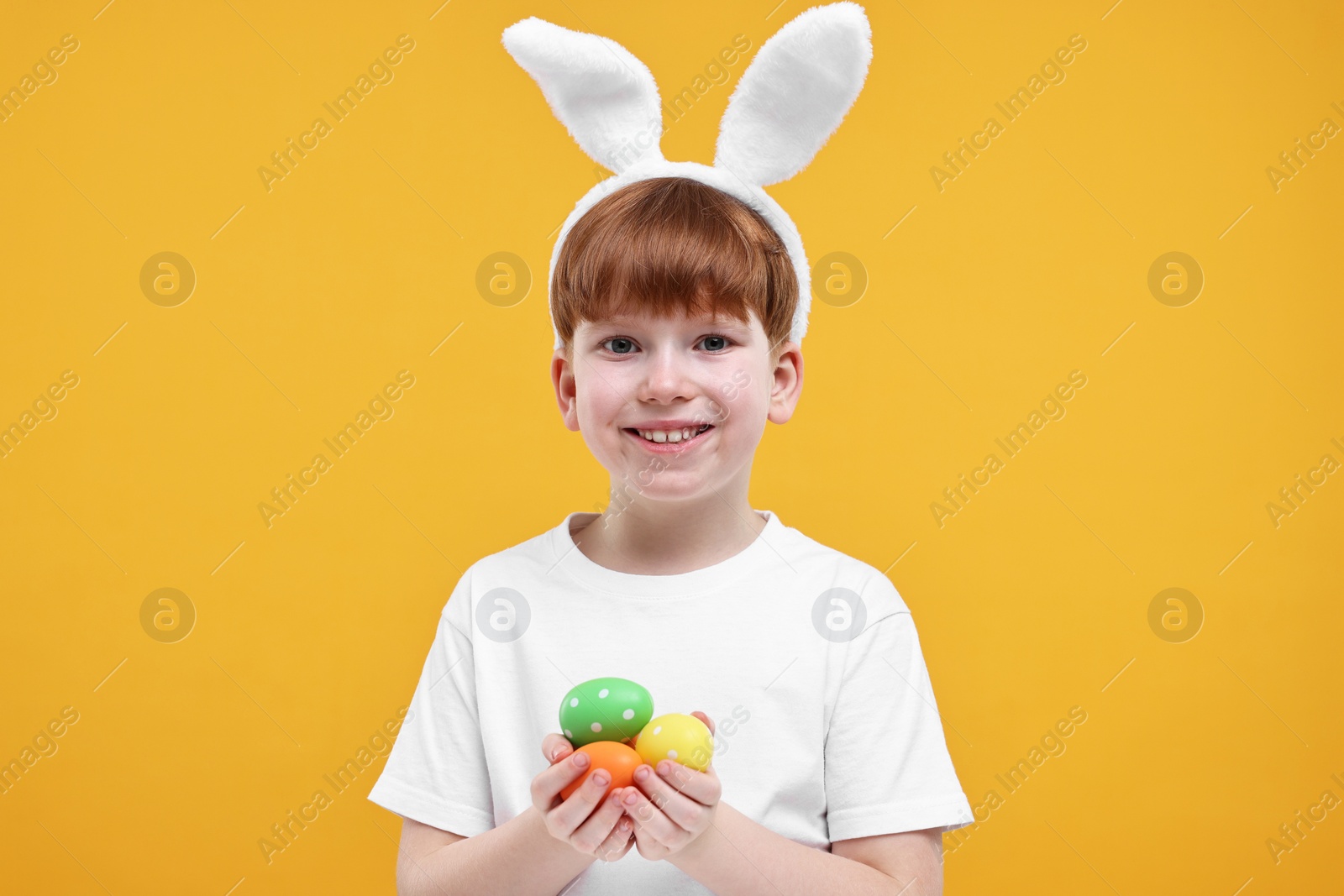Photo of Easter celebration. Cute little boy with bunny ears and painted eggs on orange background