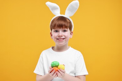 Photo of Easter celebration. Cute little boy with bunny ears and painted eggs on orange background