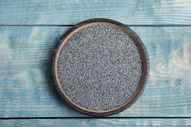 Poppy seeds in plate on wooden background, top view