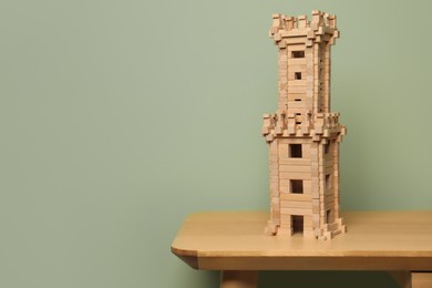 Photo of Wooden tower on table near olive wall, space for text. Children's toy