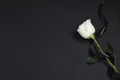 Photo of Beautiful rose and ribbon on black background, top view with space for text. Funeral symbols
