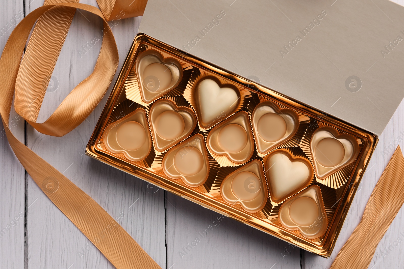 Photo of Partially empty box of chocolate candies on white wooden table, top view