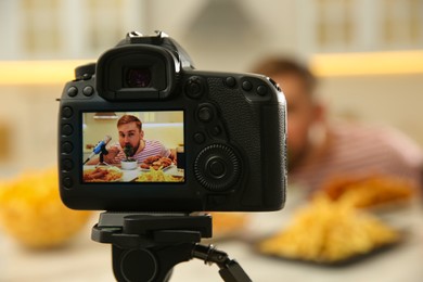 Photo of Food blogger recording eating show at table in kitchen, focus on camera screen. Mukbang vlog