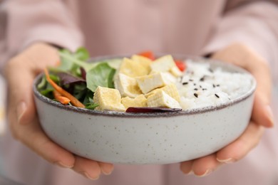 Photo of Woman holding delicious poke bowl with tofu, rice and greens, closeup