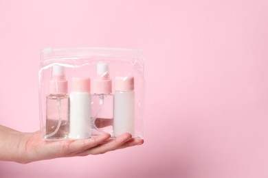 Cosmetic travel kit. Woman holding plastic bag with small bottles of personal care products against pink background, closeup. Space for text