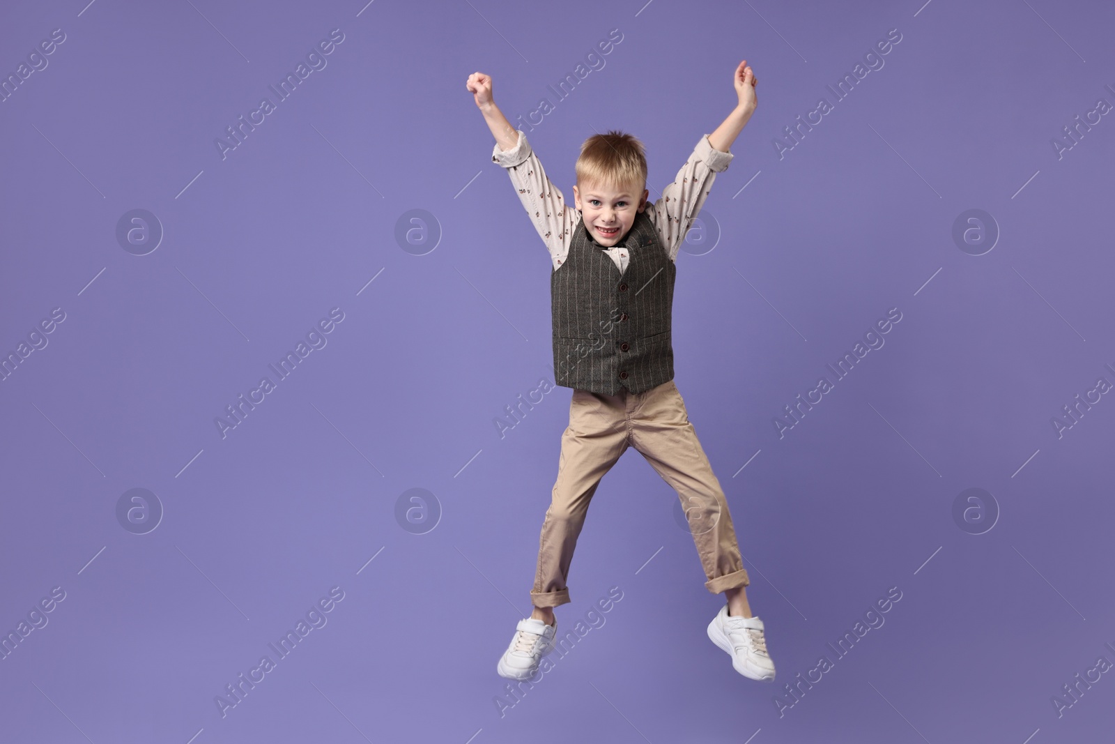 Photo of Happy little boy dancing on violet background. Space for text