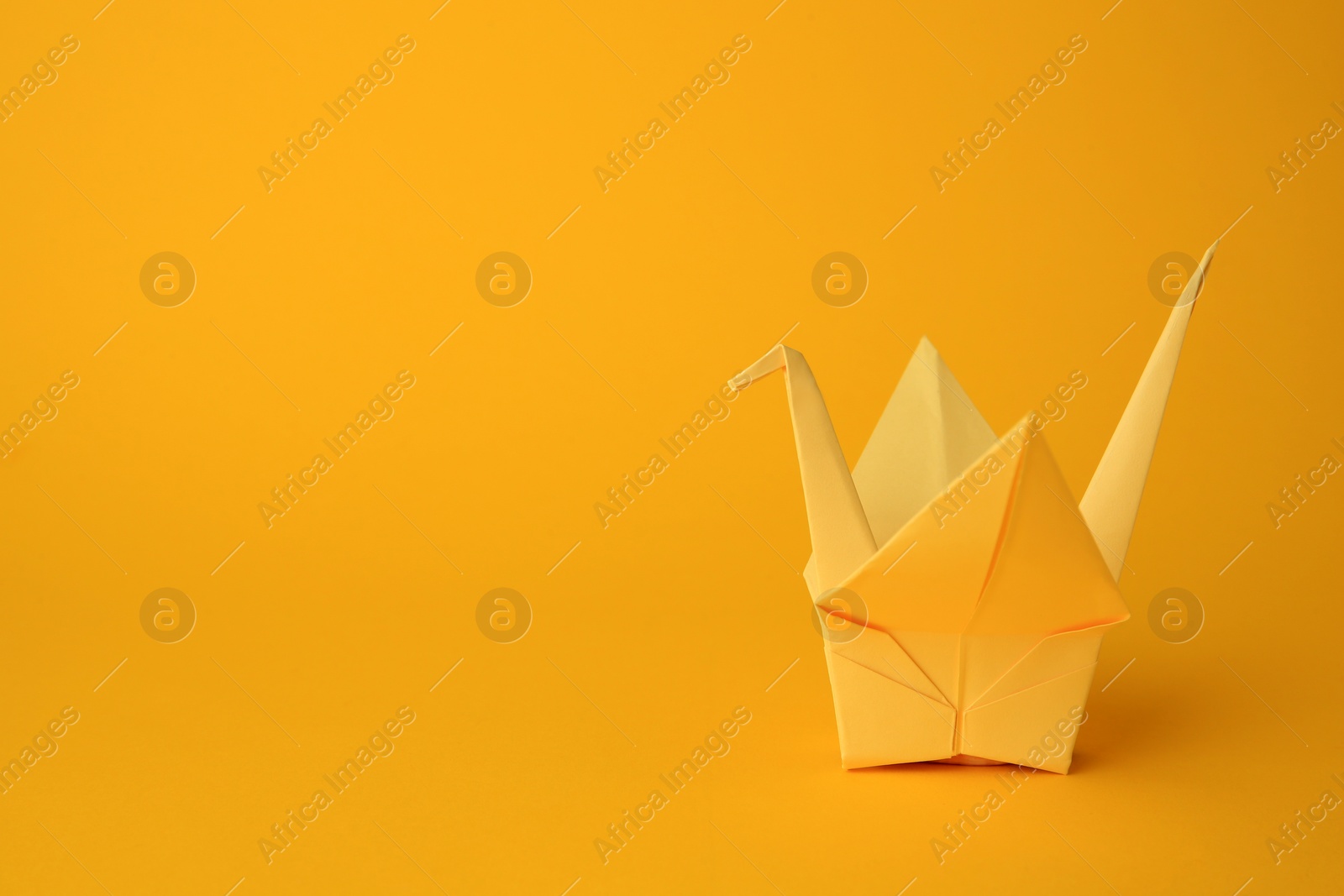 Photo of Origami art. Beautiful light yellow paper crane on orange background, space for text