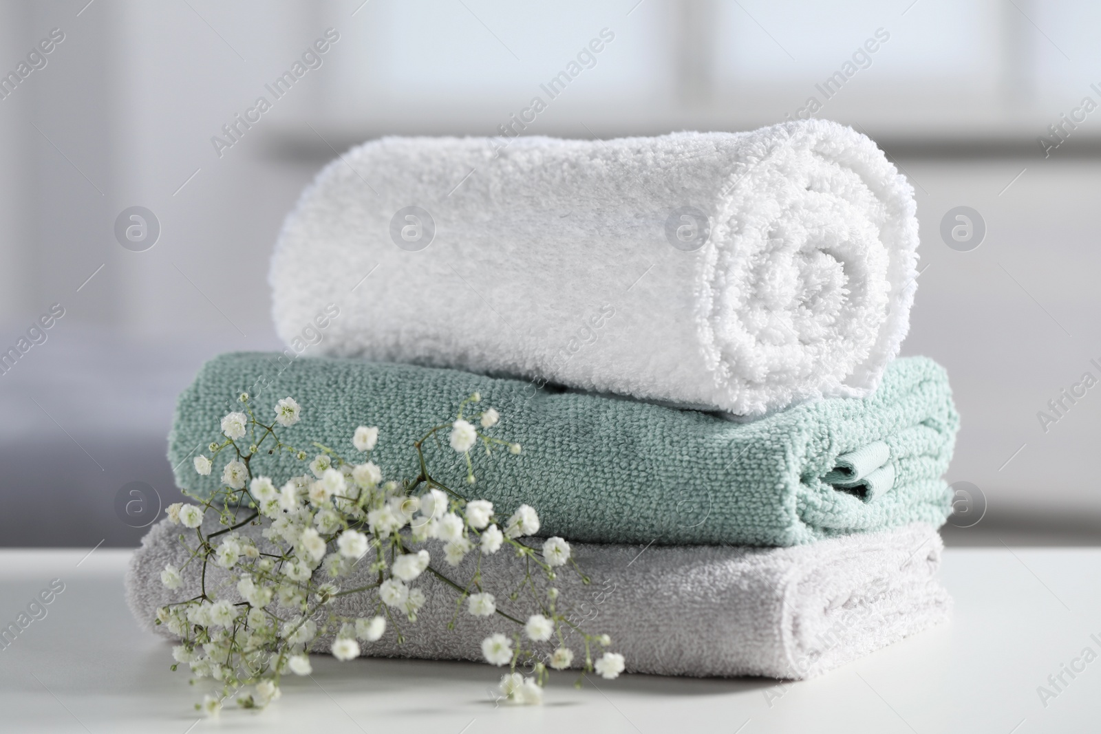 Photo of Stack of folded colorful towels with flowers on white table indoors, closeup