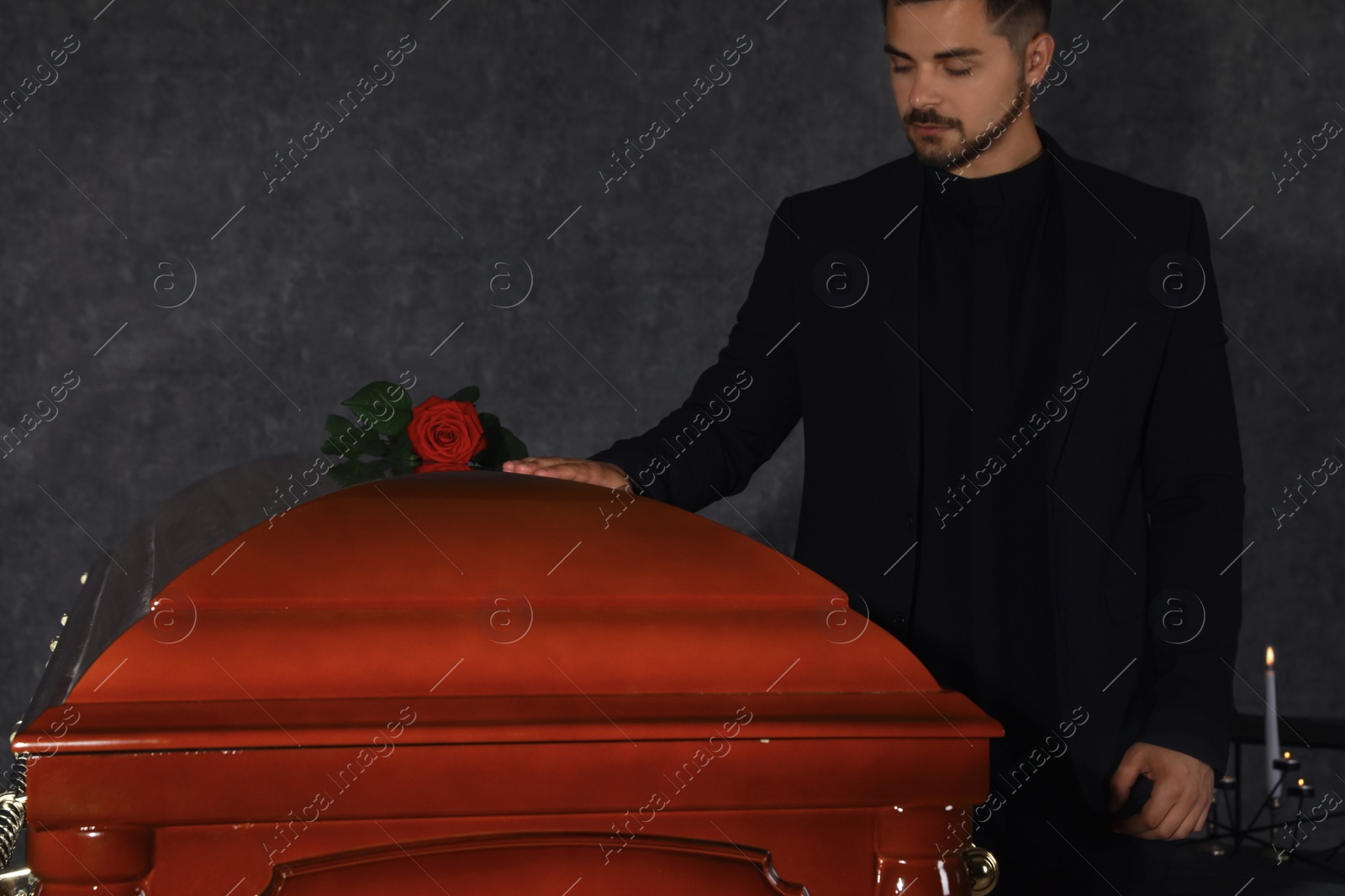 Photo of Young man near casket with red rose in funeral home, closeup