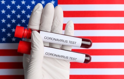 Photo of Scientist holding test tubes with blood samples over American flag, closeup. Coronavirus pandemic in USA