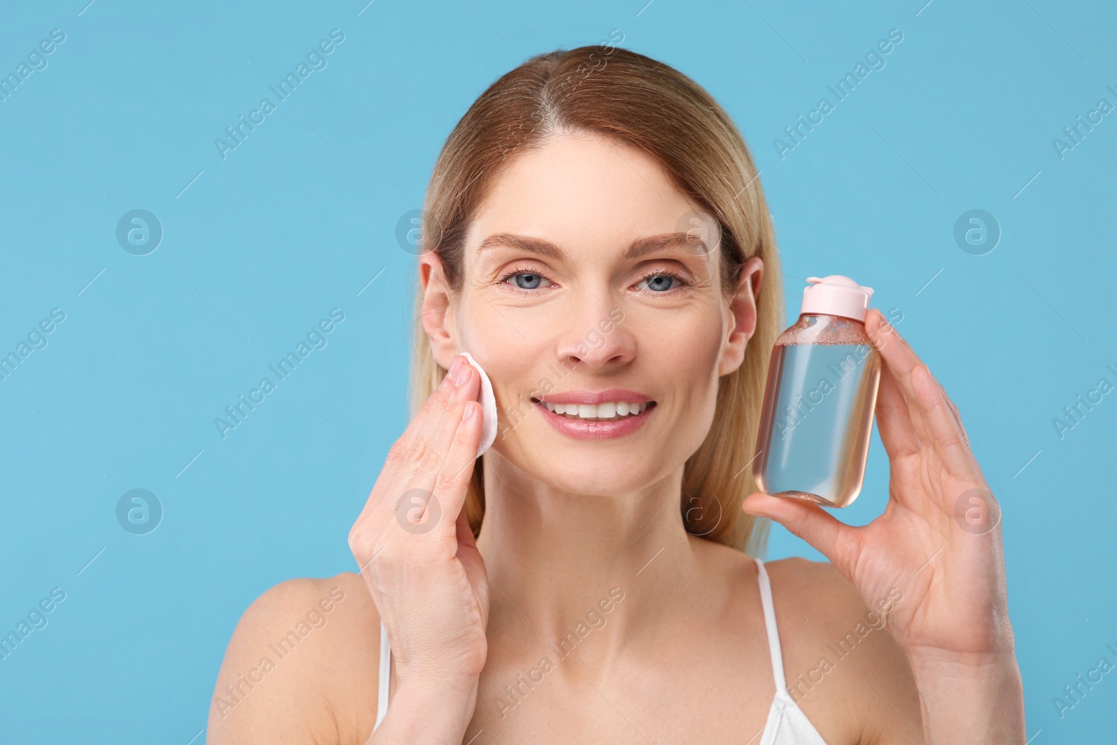 Photo of Beautiful woman removing makeup with cotton pad on light blue background