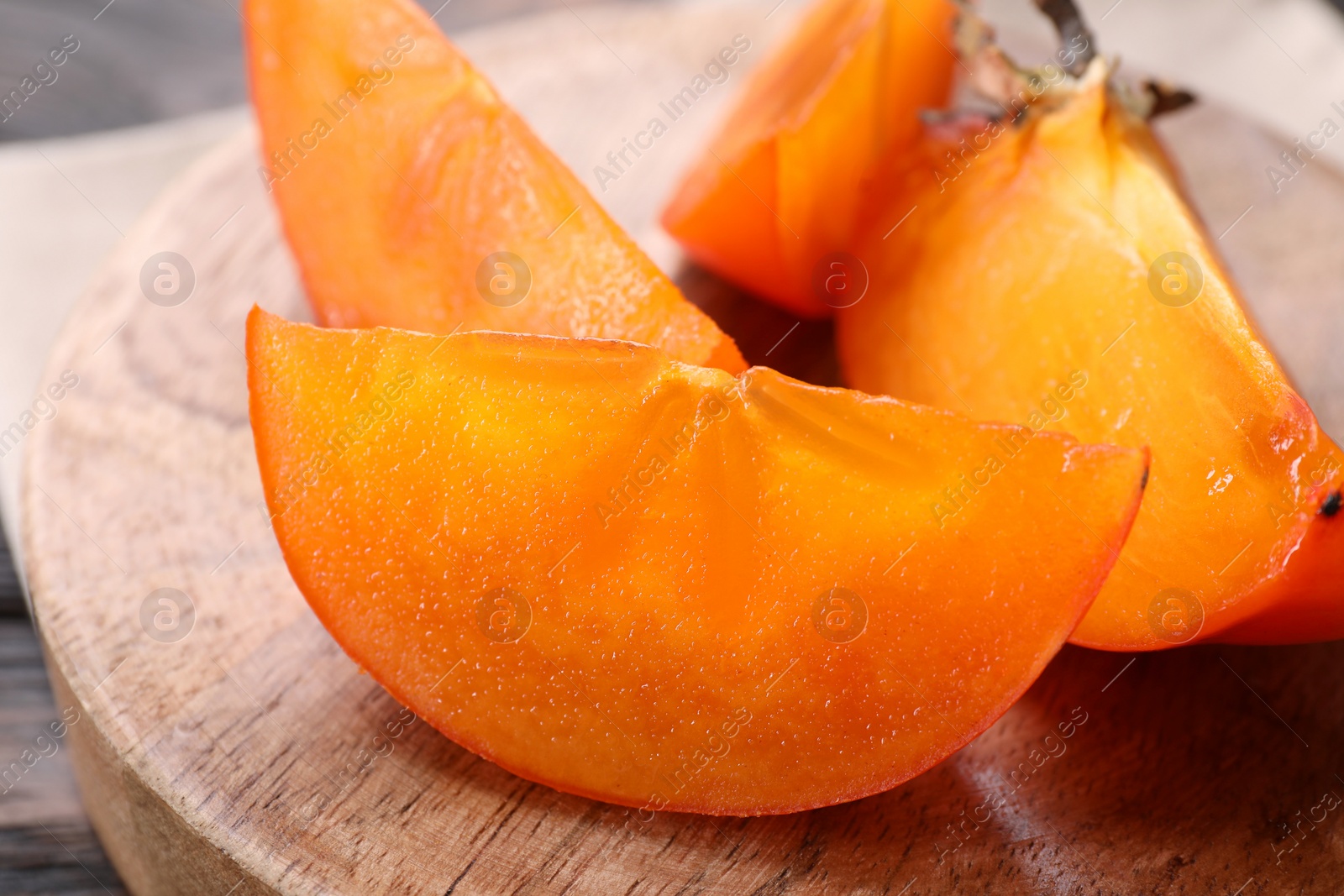 Photo of Pieces of delicious persimmons on wooden board, closeup