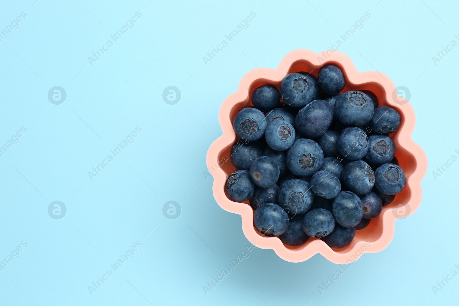 Photo of Bowl of fresh delicious blueberries on light blue background, top view. Space for text