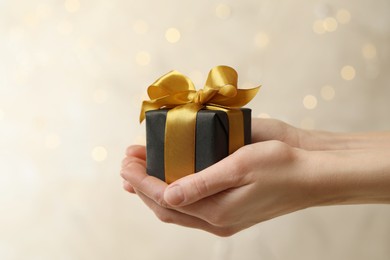 Photo of Woman holding beautifully wrapped gift box against blurred festive lights, closeup