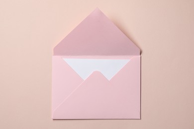 Letter envelope with card on beige background, top view