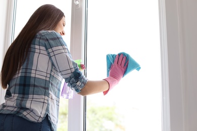 Photo of Young woman cleaning window glass at home