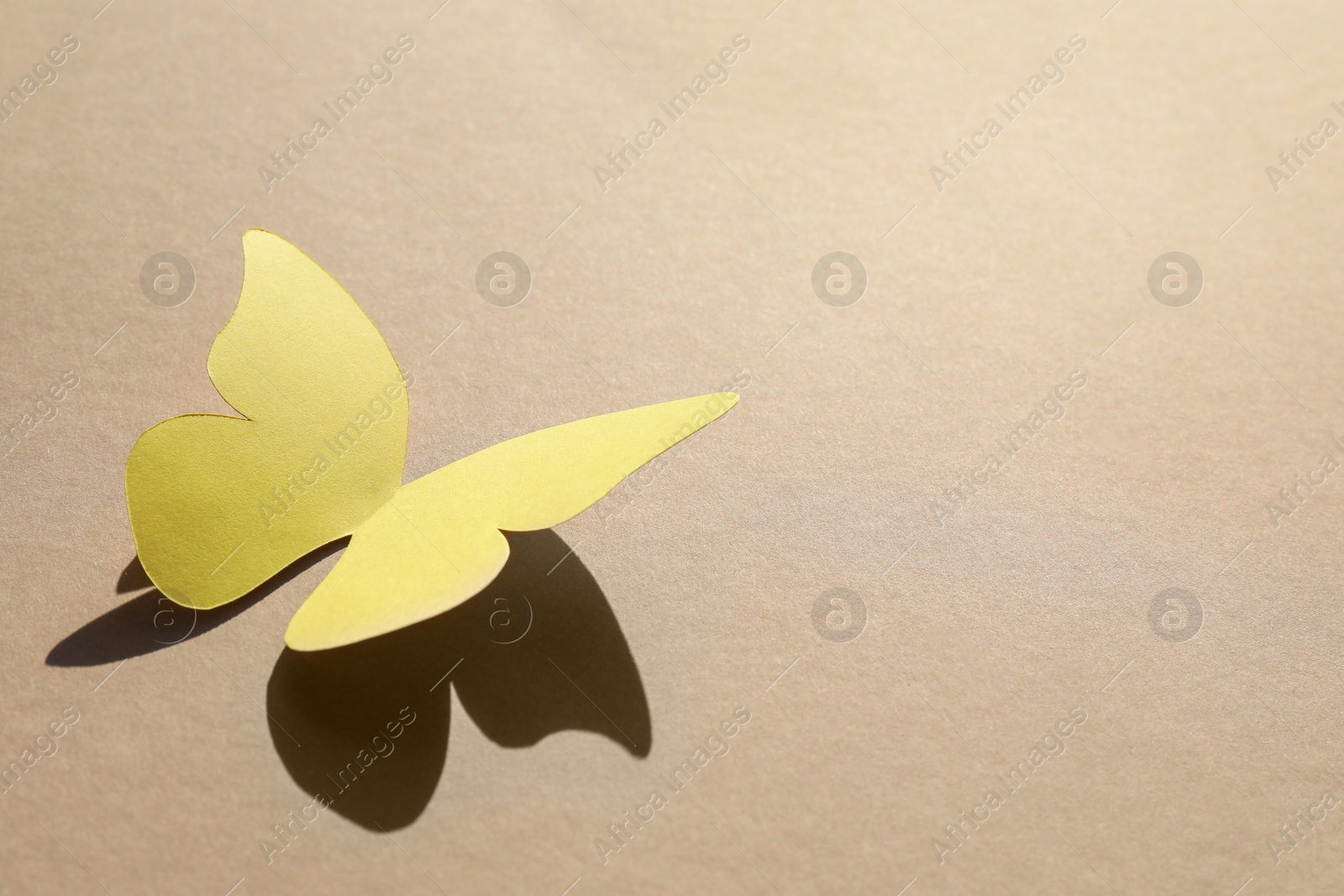 Photo of Yellow paper butterfly on light brown background, space for text