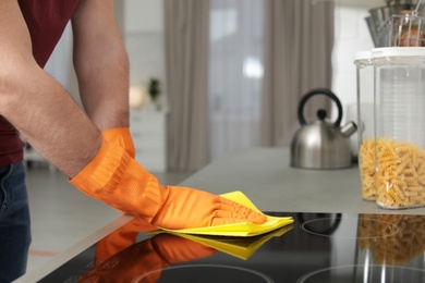 Young man cleaning oven cooktop with rag in kitchen, closeup