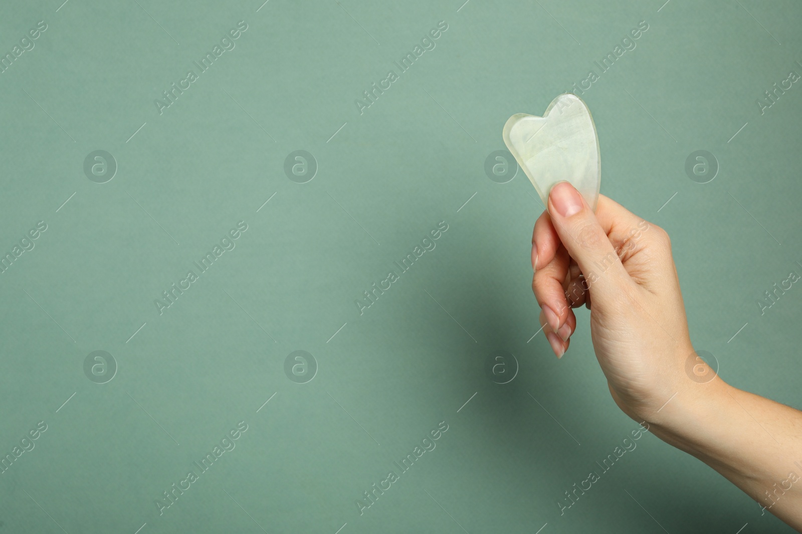 Photo of Woman with jade gua sha tool on grey green background, closeup. Space for text