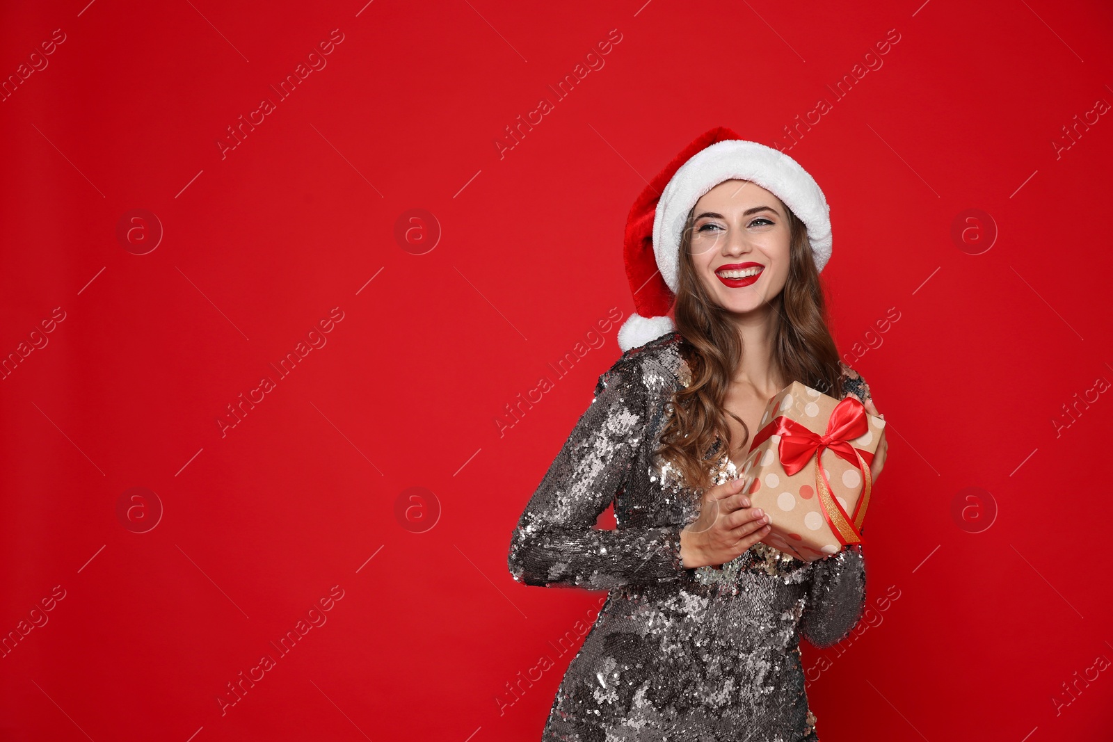 Photo of Happy woman in Santa hat with gift box on red background, space for text. Christmas party