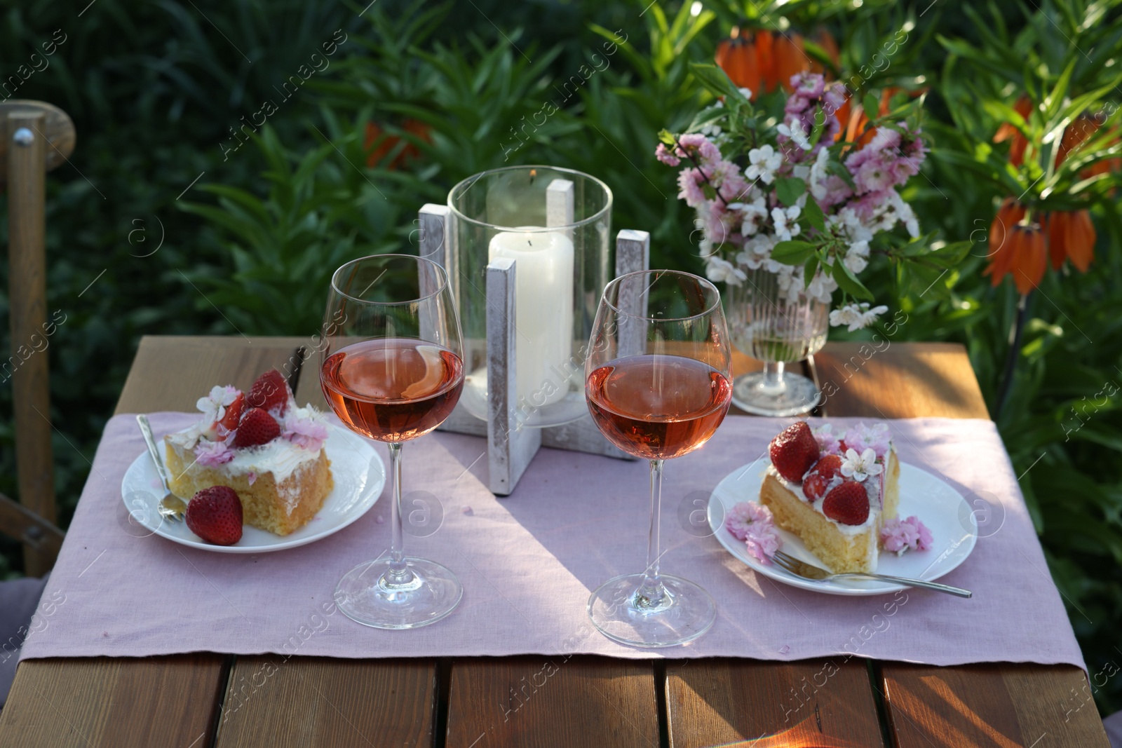 Photo of Vase with spring flowers, wine and cake on table served for romantic date in garden