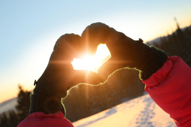 Woman making heart with hands outdoors at sunset, closeup. Winter vacation