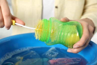 Woman washing baby bottle above basin, closeup