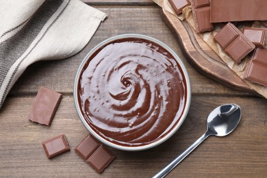 Delicious chocolate cream in bowl on wooden table, flat lay