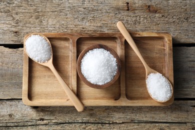 Photo of Organic salt in bowl and spoons on wooden table, top view