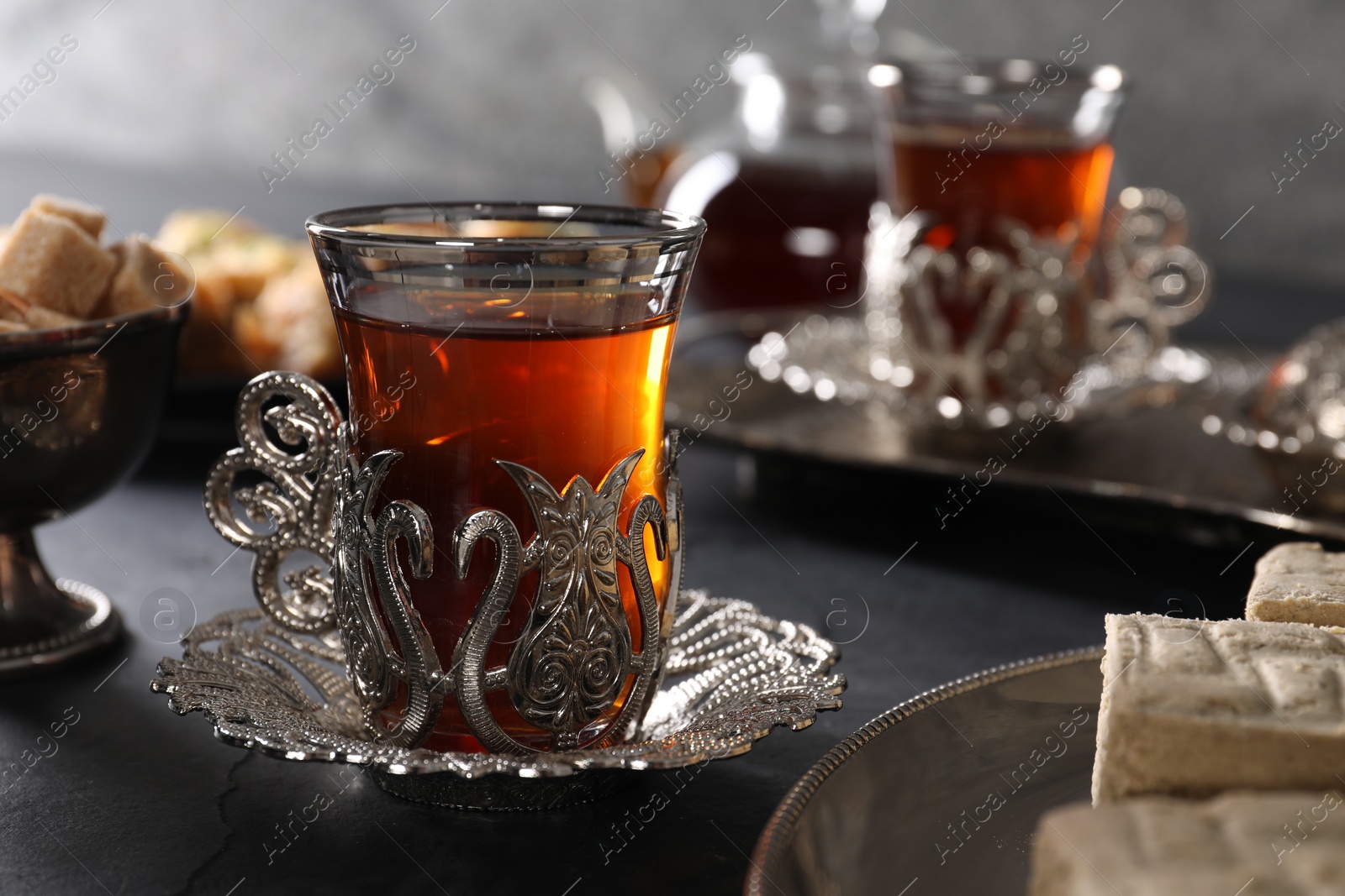 Photo of Turkish tea and sweets served in vintage tea set on black table, closeup