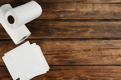 Clean napkins and rolls of paper towels on wooden table, flat lay. Space for text