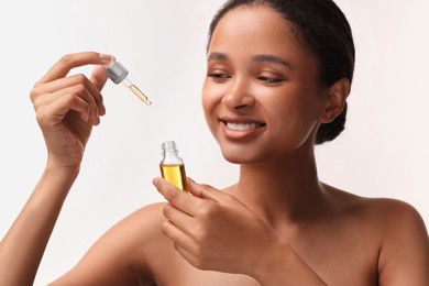 Smiling woman with bottle of serum and dropper on white background
