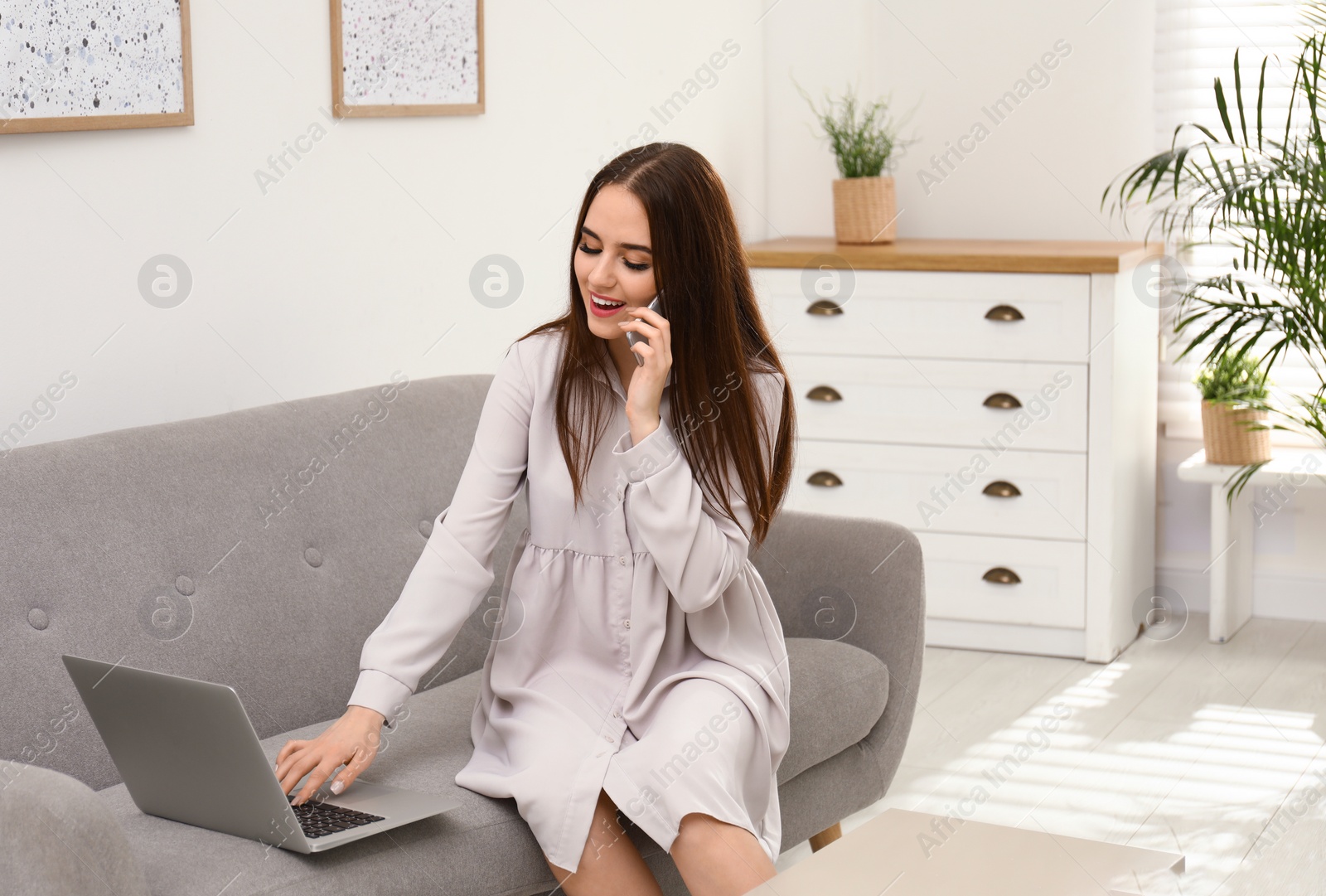 Photo of Young woman with modern laptop and mobile phone on sofa