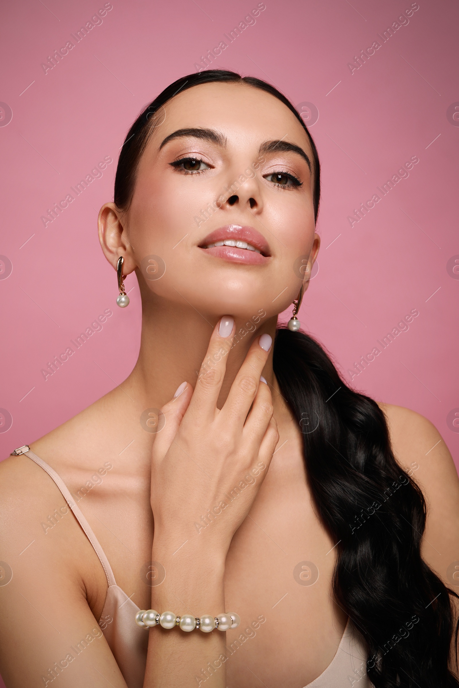 Photo of Young woman wearing elegant pearl jewelry on pink background