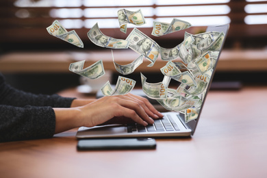 Image of Woman with modern laptop and flying dollar banknotes at table, closeup. People make money online
