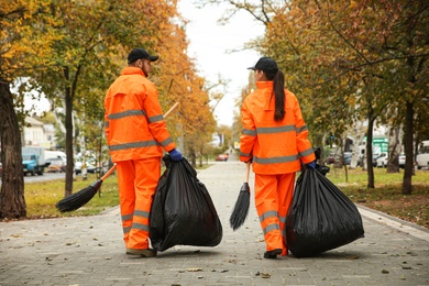 Street cleaner with brooms and garbage bags outdoors on autumn day, back view