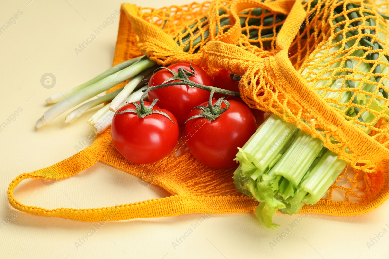 Photo of String bag with different vegetables on beige background, closeup