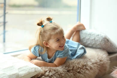 Cute little girl lying on window sill at home