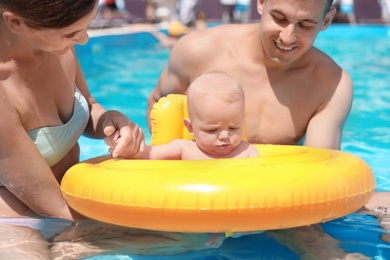 Happy parents with little baby in swimming pool on sunny day, outdoors