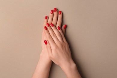 Woman with red polish on nails against beige background, closeup